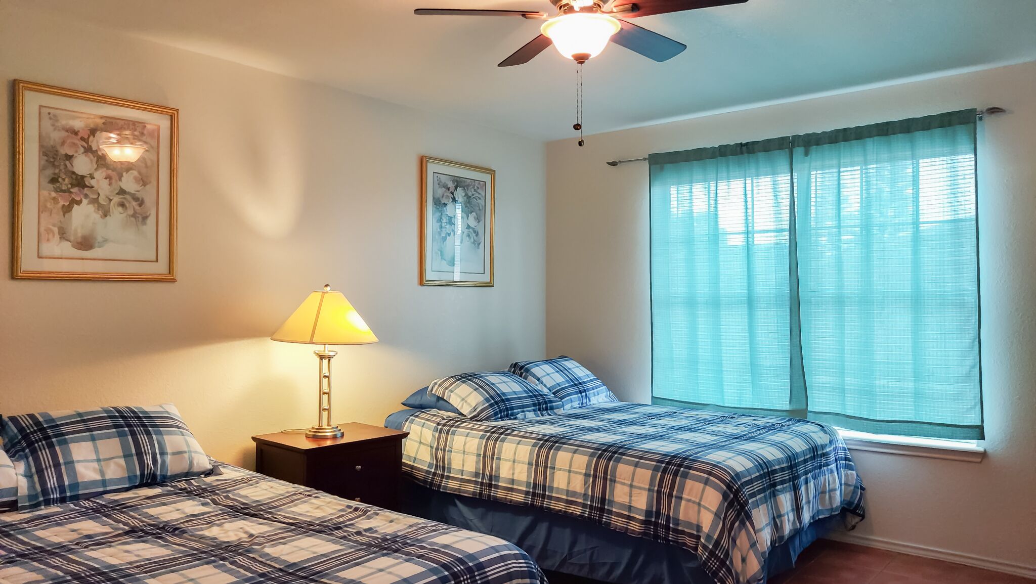 A bedroom with two beds, a nightstand, a lamp, and a ceiling fan.