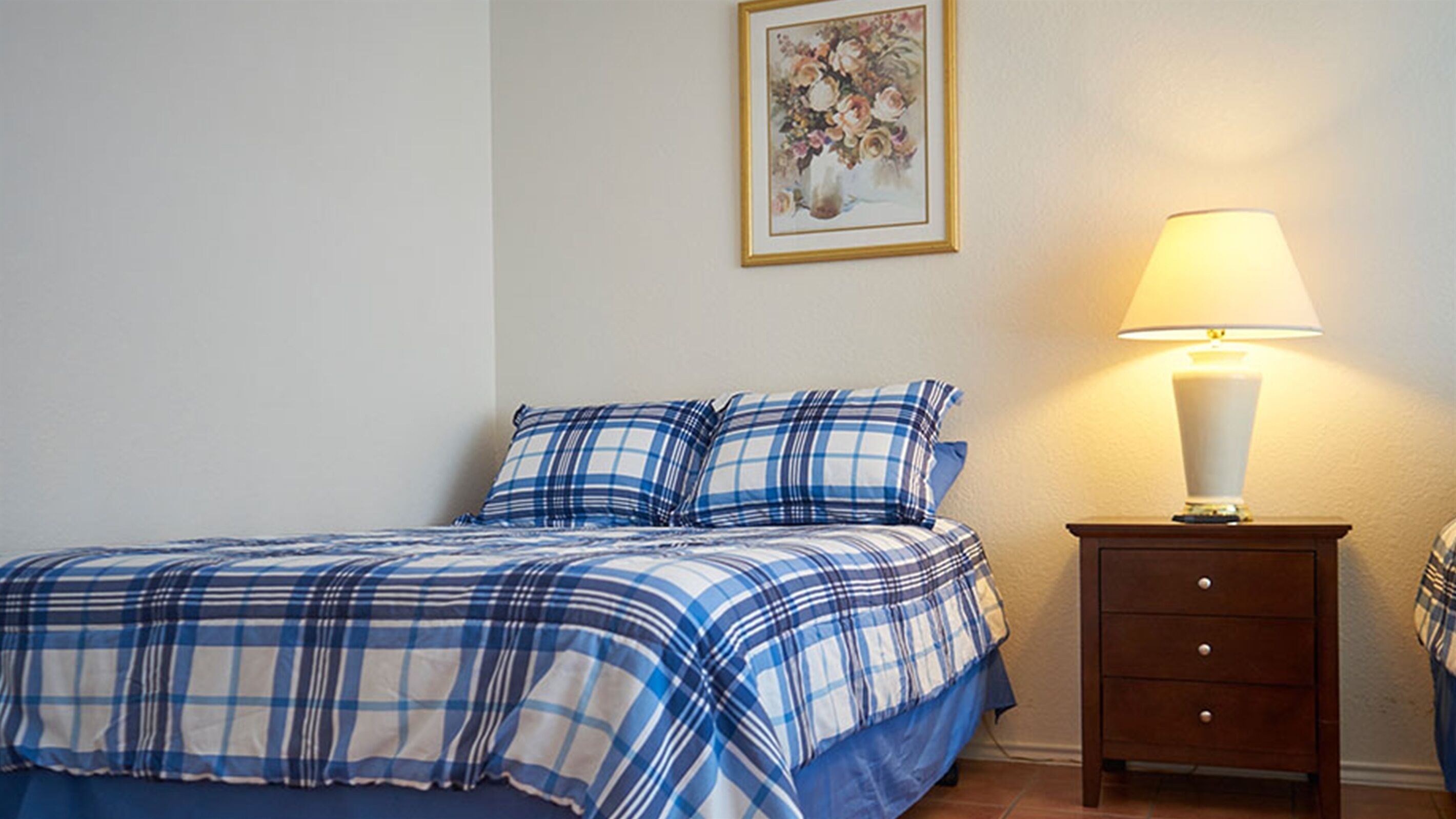A bedroom with a bed, a nightstand, a lamp, and a framed picture on the wall.