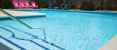 Piscina con piastrelle blu e trampolino. Sullo sfondo, sedie rosa e una recinzione in legno.