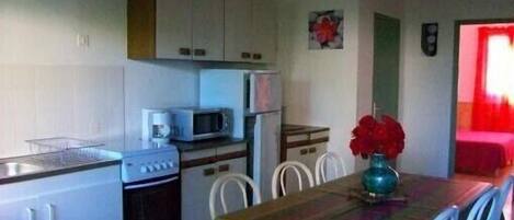 A compact kitchen with a stove, microwave, and refrigerator. There is a dining table with chairs and a vase with red flowers.