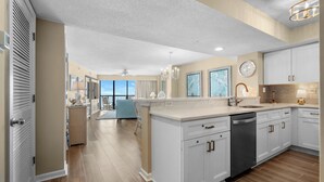 A modern kitchen with white cabinetry, a dishwasher, and a large window overlooking a balcony.