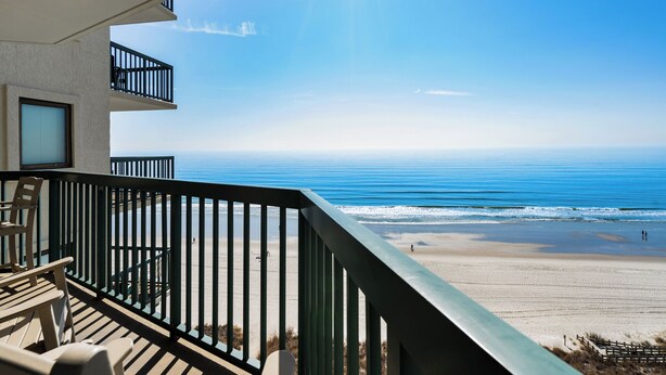 A balcony with a view of the beach and ocean.