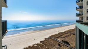 A beach view from a balcony overlooking a sandy beach with a clear sky.
