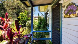 Eine überdachte Veranda mit blauer Geländer, ein Schild mit lila Blumen und üppigem Grün.
