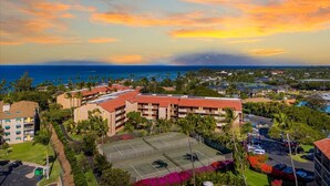 A resort with multiple buildings, a tennis court, and a view of the ocean at sunset. - Quiet, comfortable and across from gorgeous Charley Young beach  (Kihei)