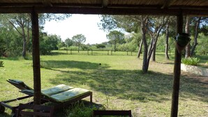 A covered outdoor seating area with a view of a grassy field and trees.