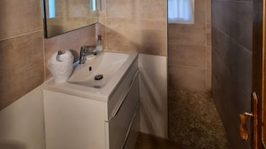 A bathroom with a wooden ceiling, a sink with a mirror, and a shower area.