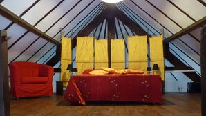 A room with a sloped ceiling, a bed with a red bedspread, a red chair, and yellow curtains.