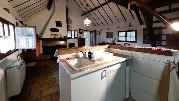 A rustic kitchen with a farmhouse aesthetic, featuring exposed wooden beams, a built-in sink, and a large window.