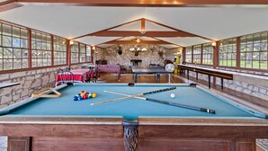Une table de billard avec des billes et des queues de billard, un mur en pierre et une cheminée en pierre.