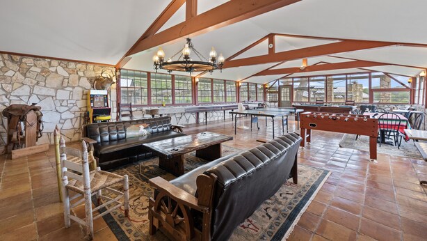 Un vaste espace intérieur doté d’un mur en pierre, de poutres en bois, d’un lustre, d’une table de billard et d’un coin salon avec un canapé et des fauteuils.