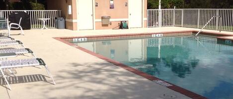 Zona de piscina con sillas de descanso, un pequeño edificio con puertas y una zona vallada.