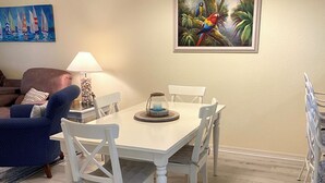 A dining area with a white table and chairs, a chandelier, a painting of tropical birds, and a lamp on a side table. - Close to Beaches, Restaurants & More!  Great Rates Too! (Bonita Springs)
