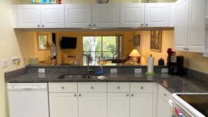 A modern kitchen with white cabinets, granite countertops, a built-in dishwasher, and a large window offering a view of the outdoors. - Close to Beaches, Restaurants & More!  Great Rates Too! (Bonita Springs)