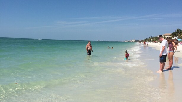 A beach scene with clear turquoise water, sandy shore, and people enjoying the beach. - Close to Beaches, Restaurants & More!  Great Rates Too! (Bonita Springs)