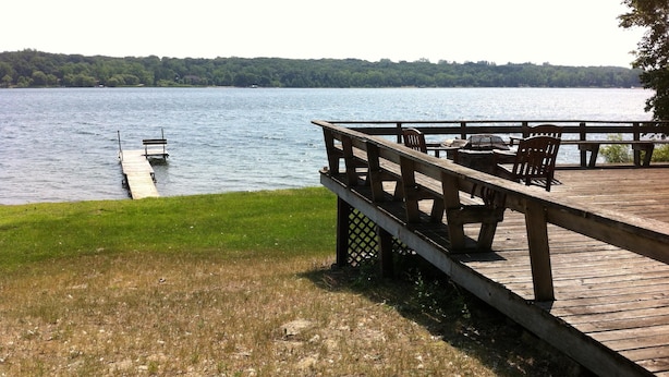 A wooden dock extending into a calm lake, surrounded by grassy banks and a forested shoreline.