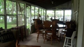 A covered porch with wooden furniture, including a sofa and chairs, and a dining table.