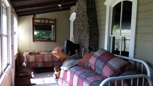 A cozy room with a bed, a couch, a television, and a stone wall.