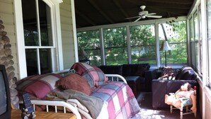 A covered porch with a bed, a chair, and a table.