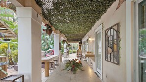 Un pasillo con plantas colgantes, un arreglo floral central y un banco a la izquierda.