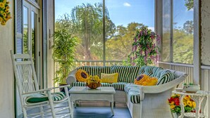 Un porche con muebles de mimbre, una mecedora y plantas en macetas.