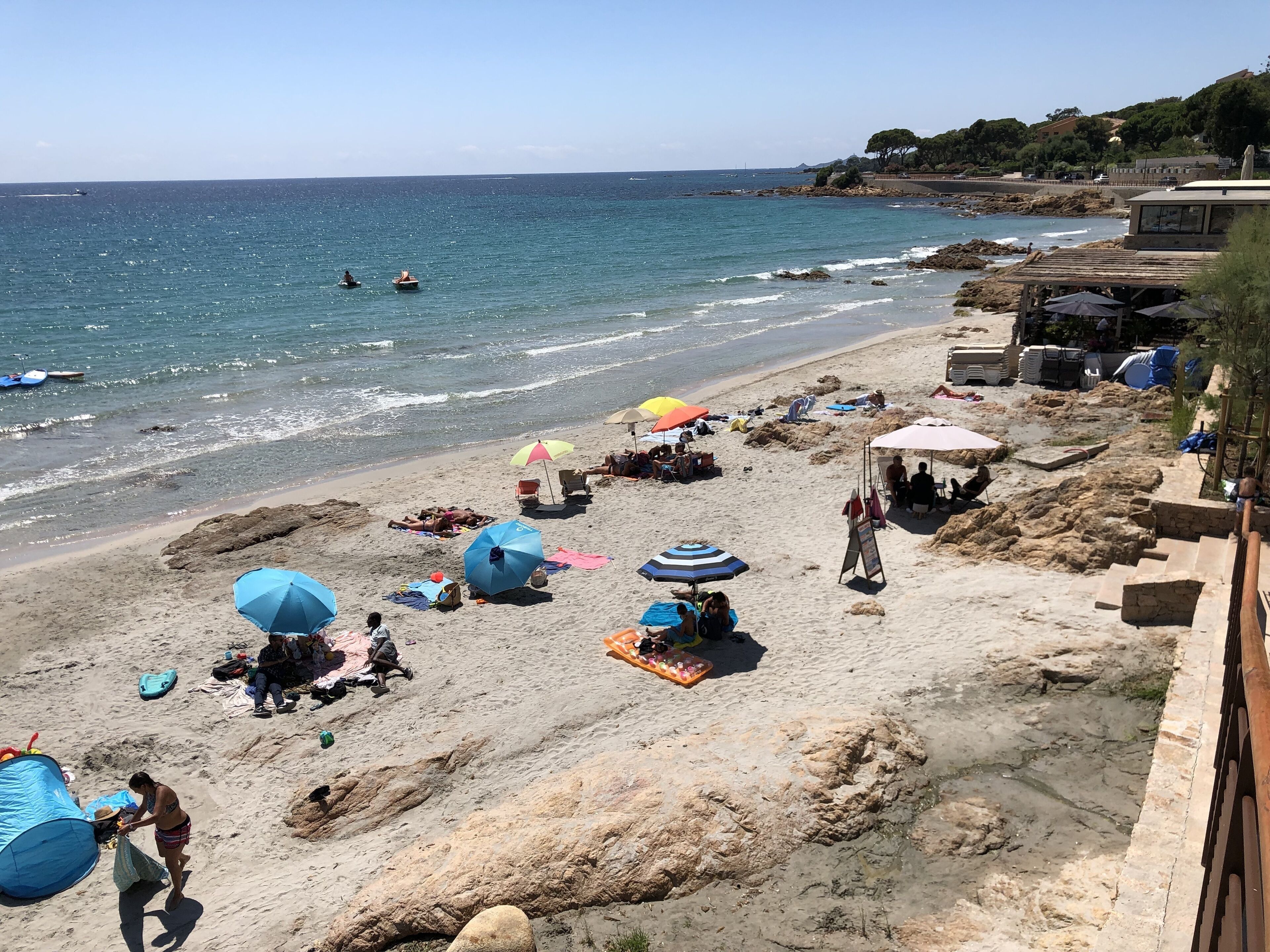 A beach with umbrellas, people, and a rocky shoreline.