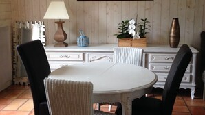 A dining area with a round table, two chairs, a lamp, a framed picture, and a vase. - Nice house classified 3 * Located in Dompierre Sur Mer, 5 Kms De La Rochelle (Dompierre-Sur-Mer)