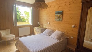 A bedroom with a bed, a chair, a window, a painting, and wooden walls. - Nice house classified 3 * Located in Dompierre Sur Mer, 5 Kms De La Rochelle (Dompierre-Sur-Mer)