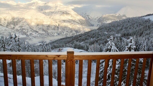 A wooden deck overlooking a snow-covered mountain landscape with dense forests.