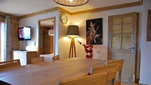 A dining area with a wooden table and chairs, a clock on the wall, a lamp, and a painting.