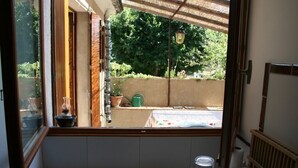 En lille balkon med udsigt over en have, en potteplante og et bord med dug.