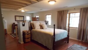 Une chambre à coucher avec un lit à baldaquin, un plancher en bois, une table de chevet, une commode et une fenêtre avec des rideaux.