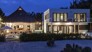 A modern beachfront property with a thatched-roof structure, a pool area, and a two-story building with large windows. - Private Luxurious Resort Right on the Ocean - Casa De Los Sueños (Puerto Escondido)
