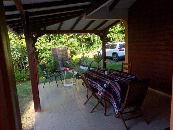 A covered patio with a table and chairs, surrounded by potted plants and a view of a parked car.