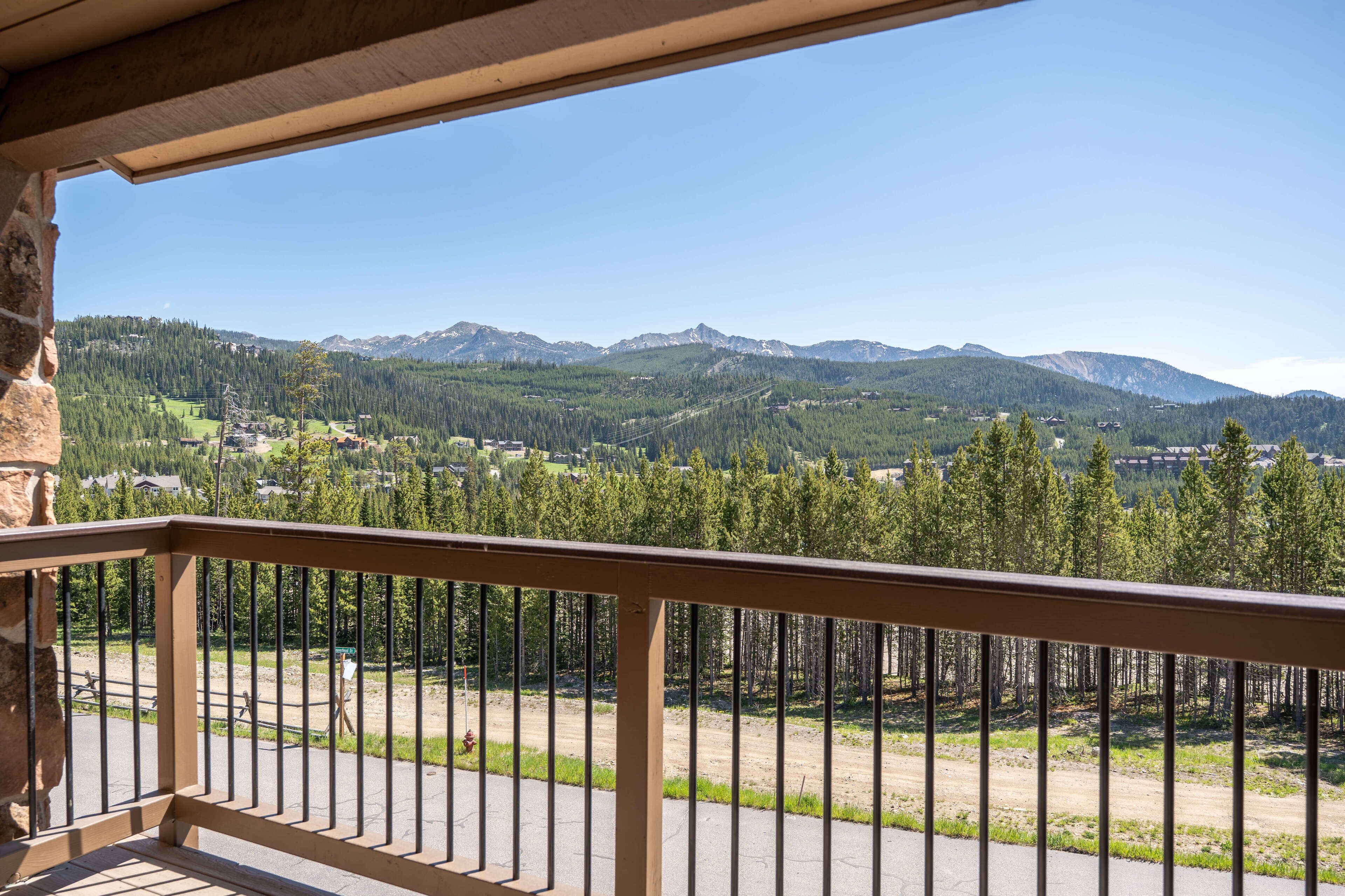 Un balcone con vista su un paesaggio montuoso, un sentiero sterrato e una zona boschiva.