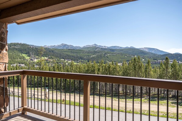 A balcony with a view of a mountainous landscape, a dirt path, and a forested area.
