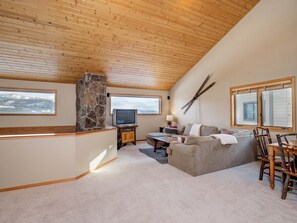 A cozy living room with a stone fireplace, a television, and a large window overlooking a snowy landscape.