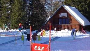 Una cabaña de madera con techo nevado, rodeada por un área cercada con un letrero que dice 