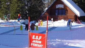 Une cabane en bois, dont le toit est recouvert de neige, entourée d’un espace délimité par une clôture et sur lequel est apposée une pancarte indiquant « E.S.F Jardin d’Enfant ».