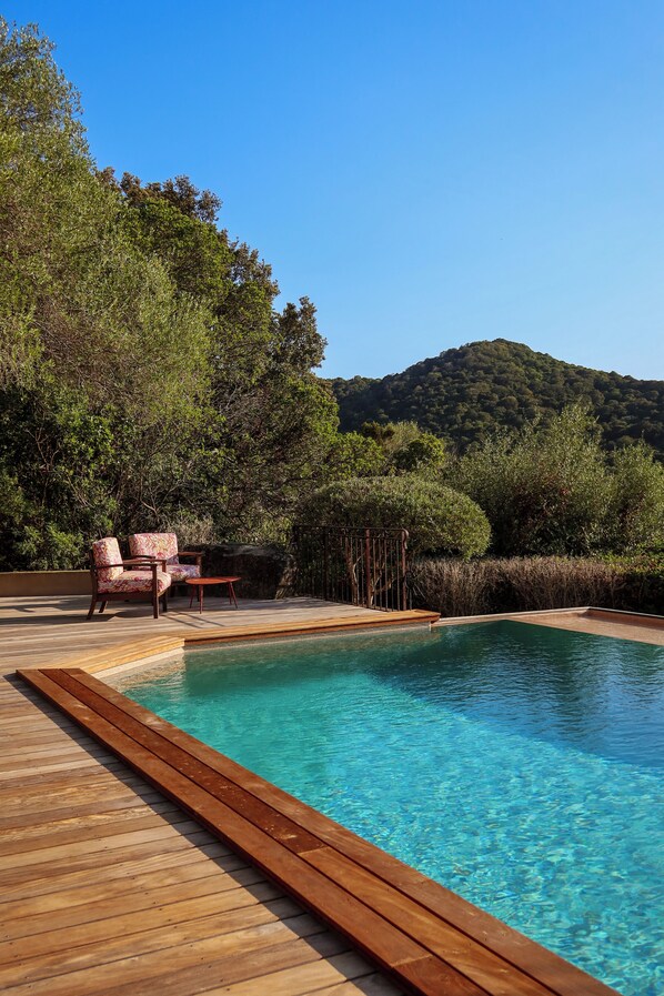 A wooden deck with a swimming pool, two chairs, and a view of a forested hill.