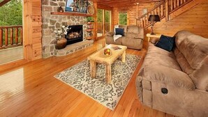 Interior acogedor de una cabaña con chimenea de piedra, muebles de madera y una escalera que lleva a un nivel superior.