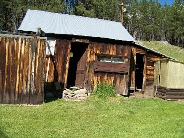 Cozy cabin nestled among trees, offering a simple retreat with a door, window, and firewood for warmth.