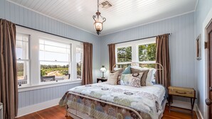 Ein Schlafzimmer mit einem großen Bett, Holzboden und Blick ins Freie durch große Fenster.
