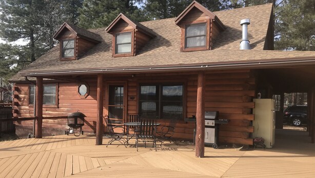 A log cabin with a porch, a grill, and a refrigerator. - Family Friendly Lakefront Cedar Log Cabin on 2 acres at Rainbow Lake. (Lakeside)