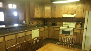 A kitchen with wooden cabinets, a white stove, and a dining table with chairs. - Family Friendly Lakefront Cedar Log Cabin on 2 acres at Rainbow Lake. (Lakeside)