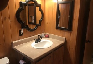 Un baño con paneles de madera, un lavamanos blanco con grifo negro y dos espejos con marcos ornamentados.