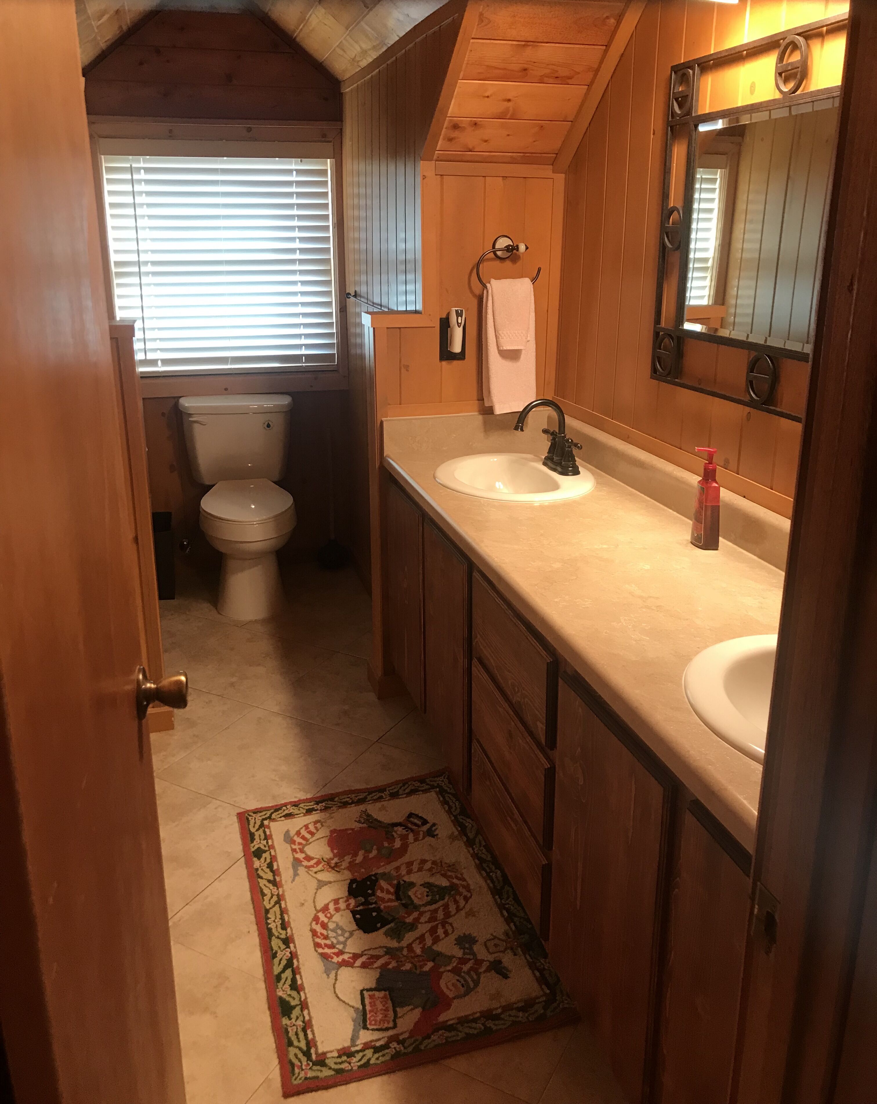Ein kleines Badezimmer mit Holzwänden, einer Toilette, zwei Waschbecken und einem Spiegel.