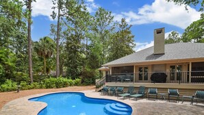 A swimming pool with a brick deck, surrounded by greenery and a covered patio area with outdoor seating. - Pet Friendly Home w/ Free Tennis & Screened Porch (Hilton Head Island)
