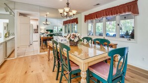 A spacious dining area with a wooden table and green chairs, a chandelier, and large windows with curtains. - Pet Friendly Home w/ Free Tennis & Screened Porch (Hilton Head Island)