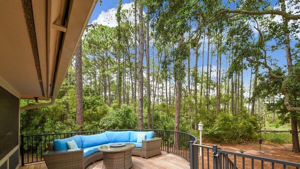 A wooden deck with a curved blue sofa and a round table, surrounded by tall trees and a metal railing. - Pet Friendly Home w/ Free Tennis & Screened Porch (Hilton Head Island)